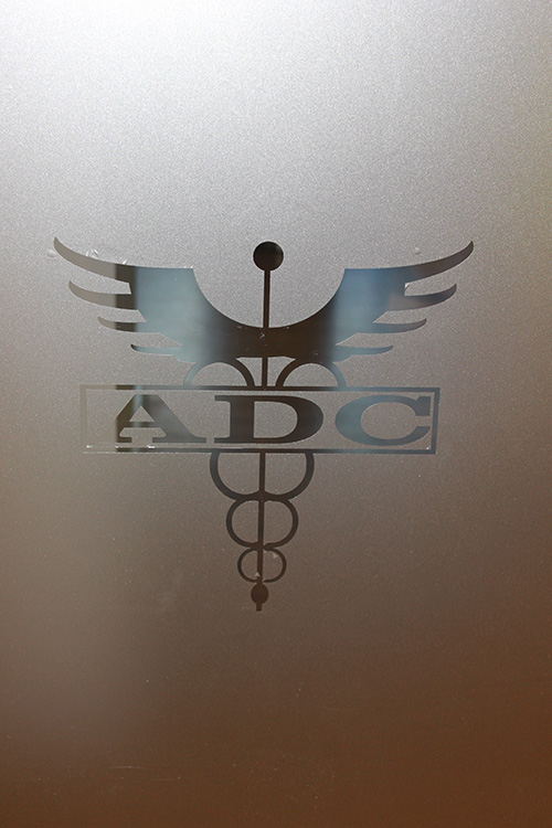 The image features a logo with the letters  ADC  prominently displayed within a shield-like emblem, set against a frosted glass background.