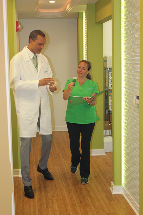 A man and woman in a hallway with green walls, the man holding a clipboard and the woman wearing a lanyard around her neck.