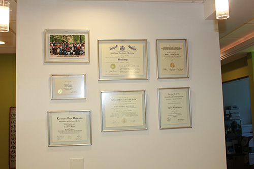 The image shows a wall with four framed certificates hanging side by side, each indicating some form of academic achievement or recognition, such as diplomas or degrees, with visible text that includes names and titles but does not provide enough detail to read in full.