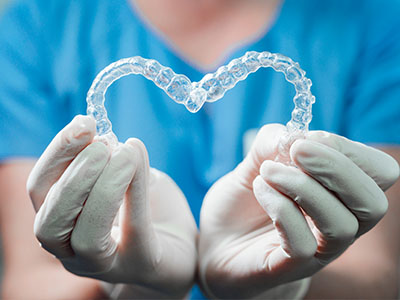 A woman s hands holding a heart-shaped piece of clear dental plastic, symbolizing dental hygiene or orthodontics.