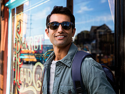 A man wearing sunglasses stands confidently next to a storefront window with a sign that reads  Secret Life.