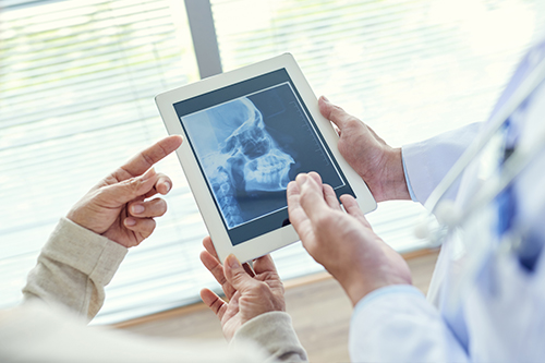 A medical professional holding a tablet with an X-ray displayed on it, showing a patient s skeletal structure, while another person looks at the screen with interest.