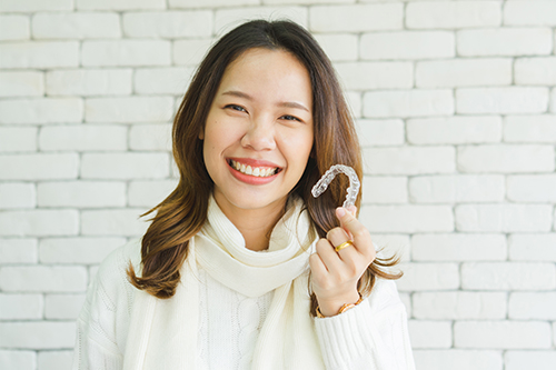 A smiling woman holding up a toothbrush with her right hand.