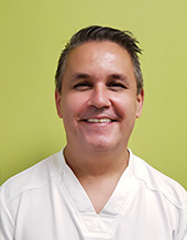 The image shows a man wearing a white lab coat standing in front of a green background.