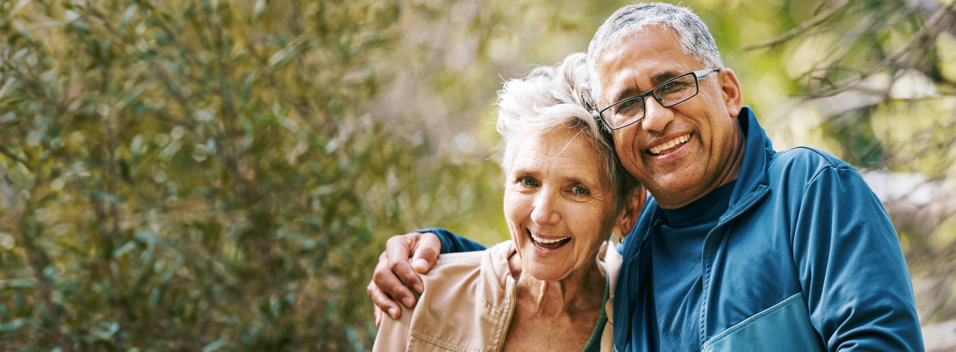 An elderly couple hugging each other outdoors.