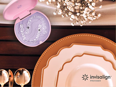 A photograph of a table setting with various plates, cutlery, and a decorative box containing dental floss, set against a wooden table with a pink lid in the foreground.