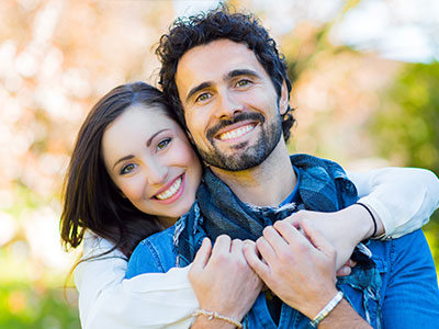 A man and woman are hugging each other closely, both smiling and appearing happy.