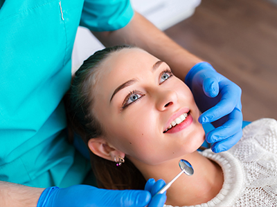 A woman receiving dental care from a professional, with her mouth open and a dental tool near her teeth.