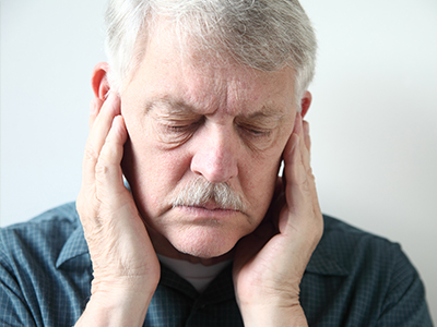 The image shows an older man with his eyes closed, holding his hand over his ear, seemingly in pain or discomfort.